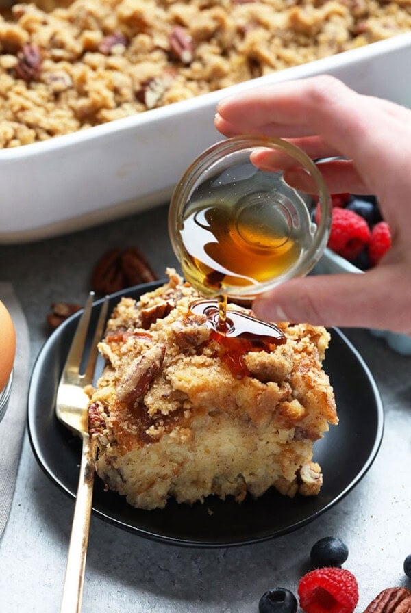 A person is drizzling honey on a piece of bread for an Overnight French Toast Bake.
