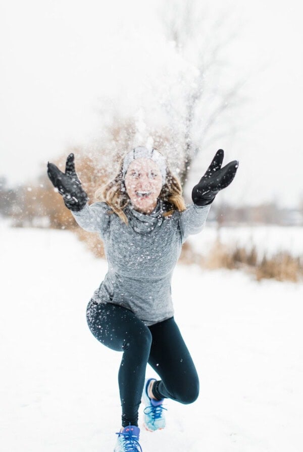 a woman, with a determined mindset, squats down and throws snow into the air.