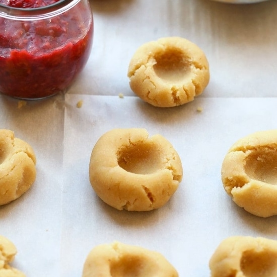 Raspberry Thumbprint Cookies on a baking sheet with a bowl of jam.