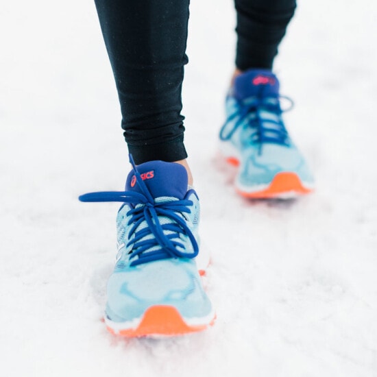 A woman showcasing her running mindset in blue and orange shoes on the snowy ground.