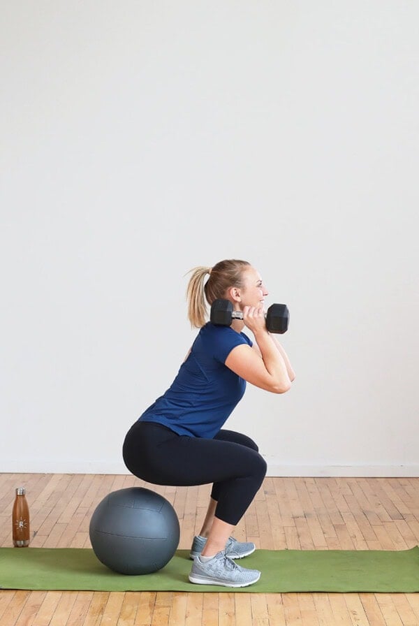 A woman performing squats with dumbbells on an exercise ball as part of her no treadmill interval cardio workout.