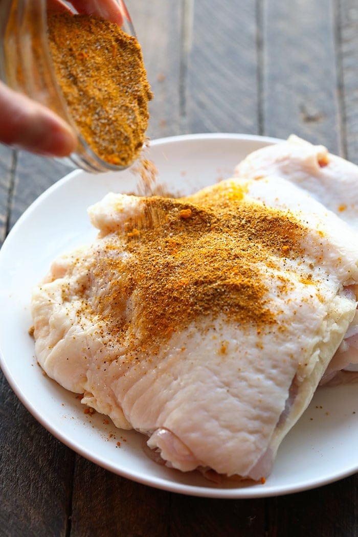 Pouring dry rub onto chicken thighs
