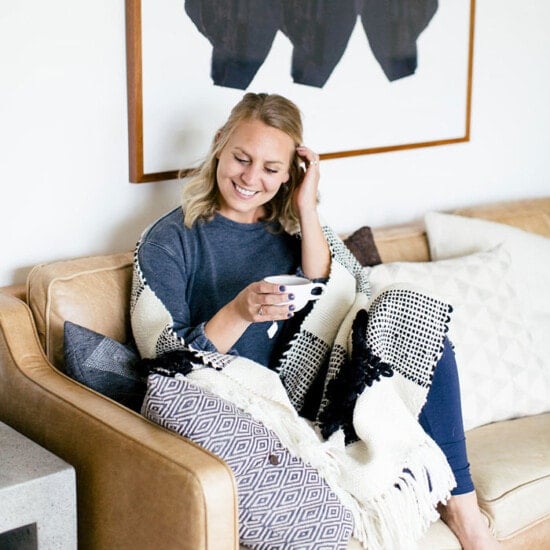 A woman cozily lounges on a couch wrapped in a blanket.