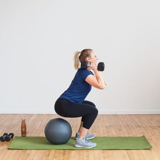 A woman performing squats with dumbbells on an exercise ball as part of her no treadmill interval cardio workout.