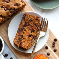 A slice of carrot cake paired with a cup of coffee on a cutting board.
