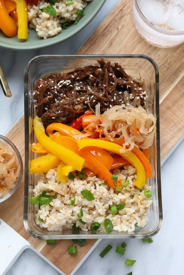 A glass container filled with Instant Pot Korean Beef accompanied by rice, peppers, and carrots.