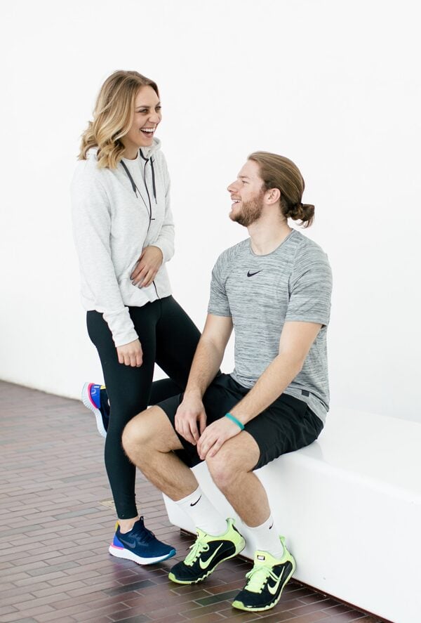 A woman wearing Nike Epic React sneakers and a man sitting on a white bench.
