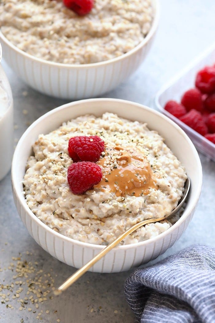 Avena cortada en acero en un tazón con mantequilla de nueces y frambuesas