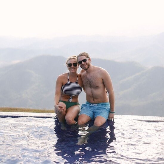 A man and woman sitting in a Costa Rican pool with mountains in the background.