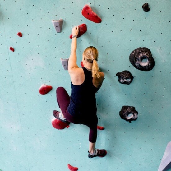 a vulnerable woman scaling a rock wall in a gym.