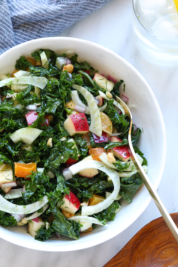 A bowl of kale salad with apples and onions.