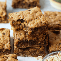 a stack of peanut butter cookie bars with a bowl of oats.