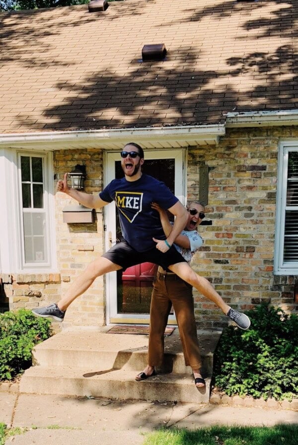 A couple jumps happily in front of the house they just bought.
