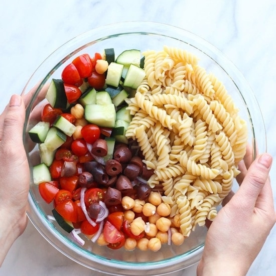 A person holding a bowl of Greek pasta salad.