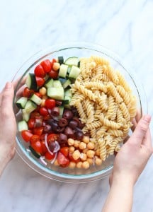 A person holding a bowl of Greek pasta salad.