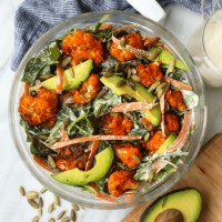 a bowl of salad with avocado, carrots and Buffalo Cauliflower.