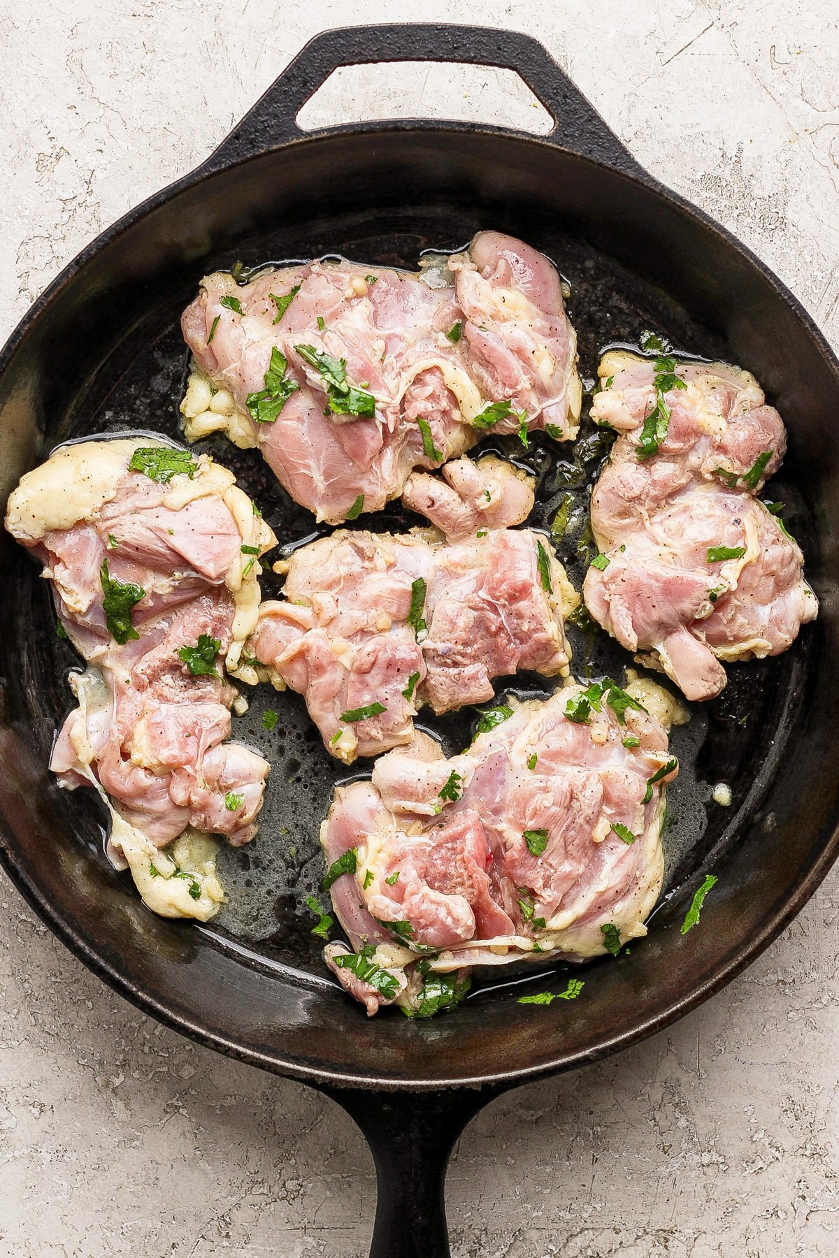 Raw marinated chicken pieces with herbs placed in a black cast iron skillet on a light countertop, perfect for easy chicken meal prep.