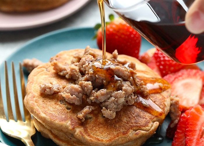Maple breakfast sausage pancakes on a plate with syrup poured over the stack.