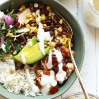 a bowl with bbq chicken, rice, beans, corn, and avocado.