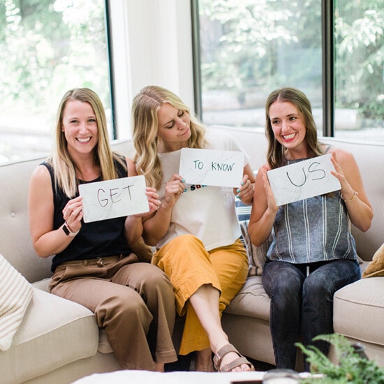 Three fit women sitting on a couch showcasing signs.