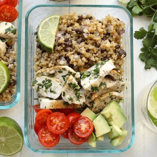 A glass container with cilantro lime chicken, rice, avocado, tomatoes and limes.