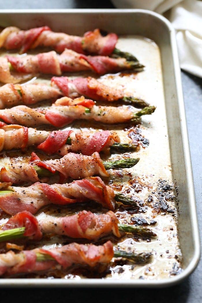 This Bacon Wrapped Asparagus Recipe is perfect for a tasty side dish or appetizer! Bacon wrapped asparagus on a baking sheet