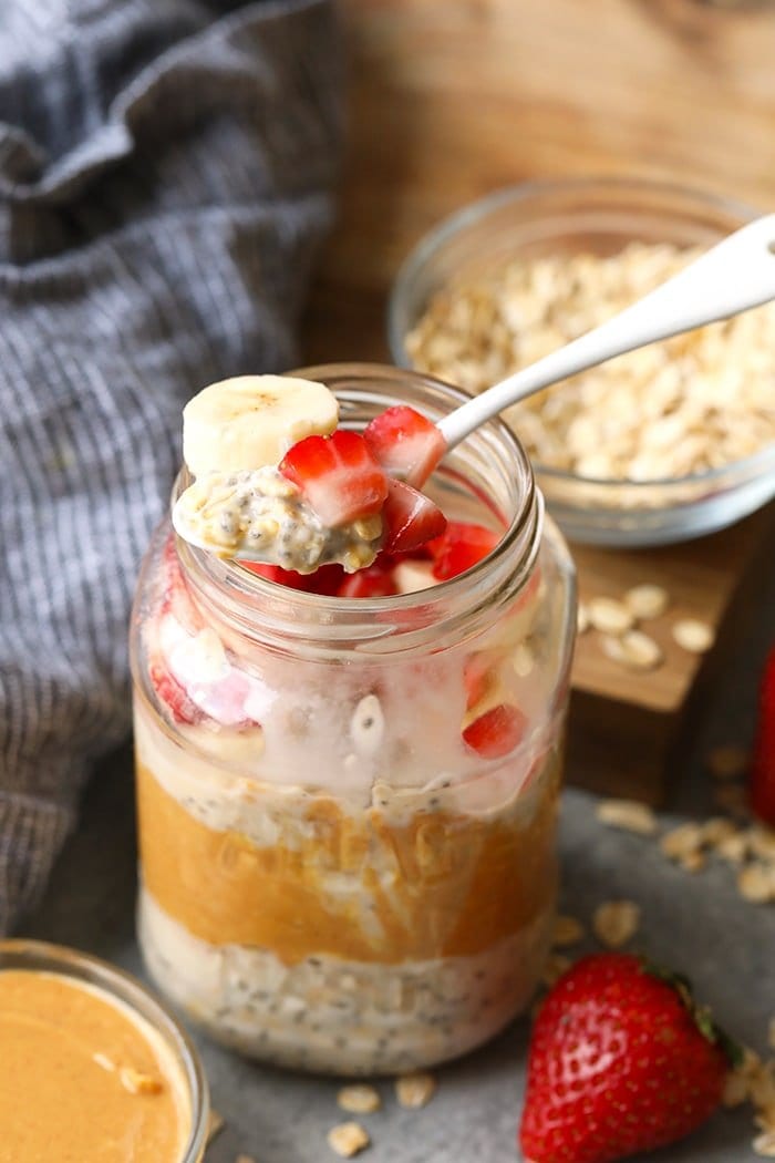 Vegan overnight oats topped with strawberries and bananas on a spoon.