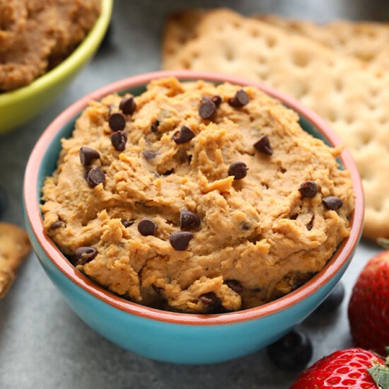 A bowl of peanut butter hummus with strawberries and crackers, topped with edible cookie dough.