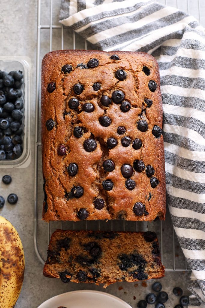 Perfectly moist blueberry banana bread made with whole grains, Greek yogurt, fresh blueberries, and maple syrup! banana bread loaf on a cooling rack.