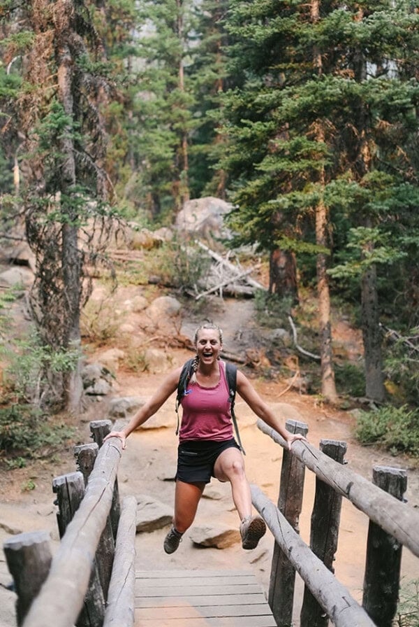 a woman jumping over a wooden bridge in the woods.