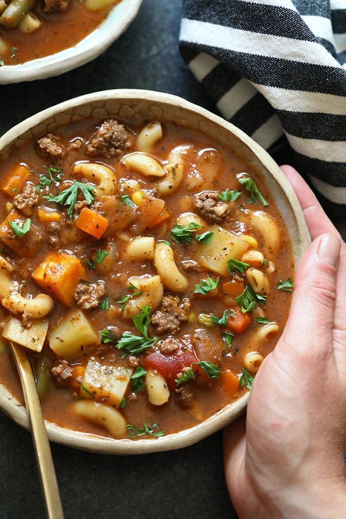 A hand holding a bowl of hamburger soup