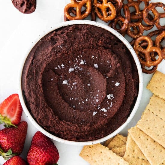 a bowl of edible cookie dough dip next to pretzels and strawberries.