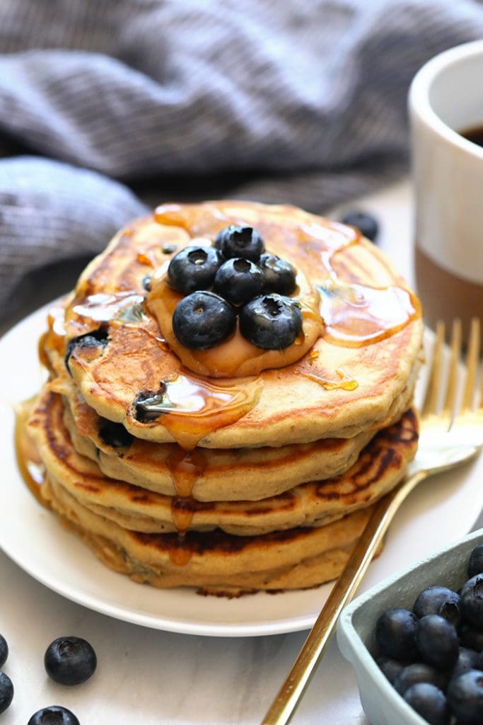 a stack of blueberry pancakes on a plate with a cup of coffee.
