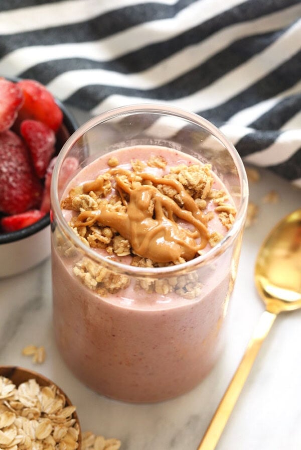 A breakfast bowl with strawberry oatmeal topped with granola and peanut butter.