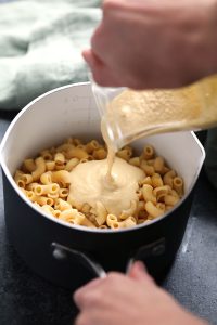 a person pouring a vegan sauce over pasta in a pan.