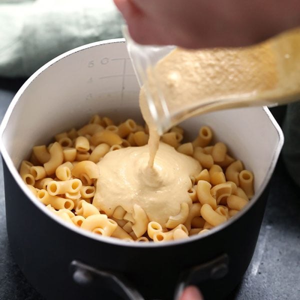 a person pouring a vegan sauce over pasta in a pan.