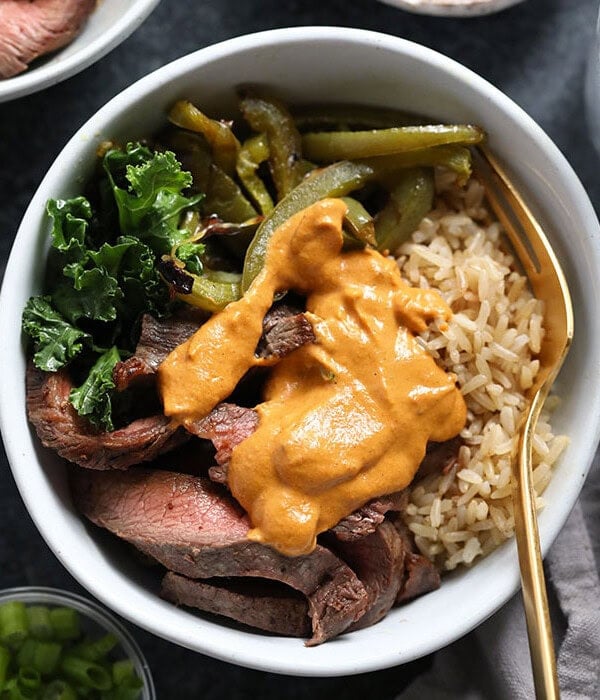 A bowl featuring Philly cheese steak alongside green beans and rice.