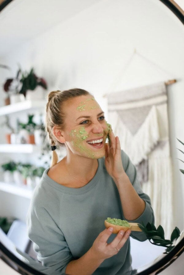 A woman wearing a green face mask at home, admiring herself in front of the mirror.