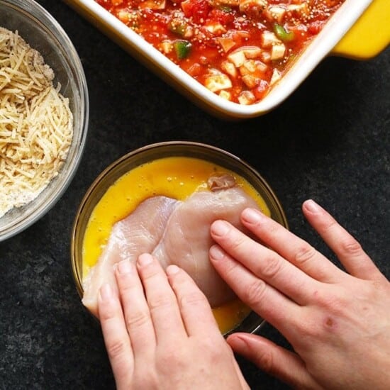 A person's hand reaches into a dish of healthy chicken parmesan.