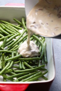 A healthy casserole of green beans with a sauce being poured over them.