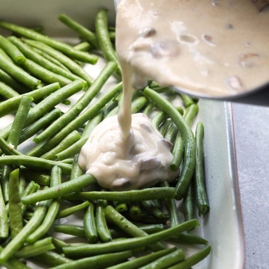 A healthy casserole of green beans with a sauce being poured over them.
