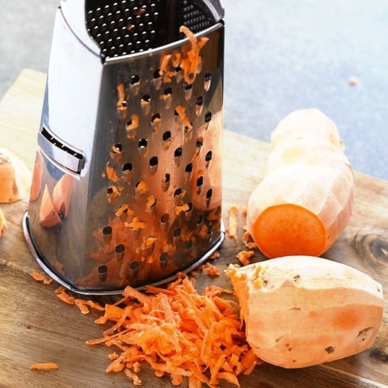 A cutting board with sweet potato hash browns being grated.