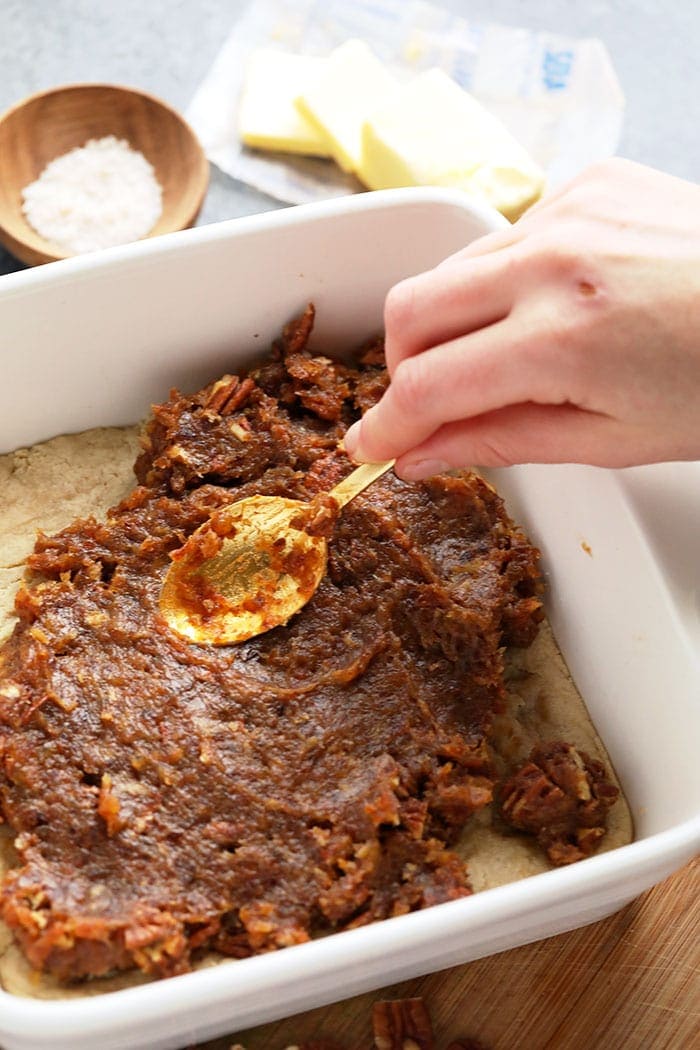 A hand spreading date caramel over short bread crust