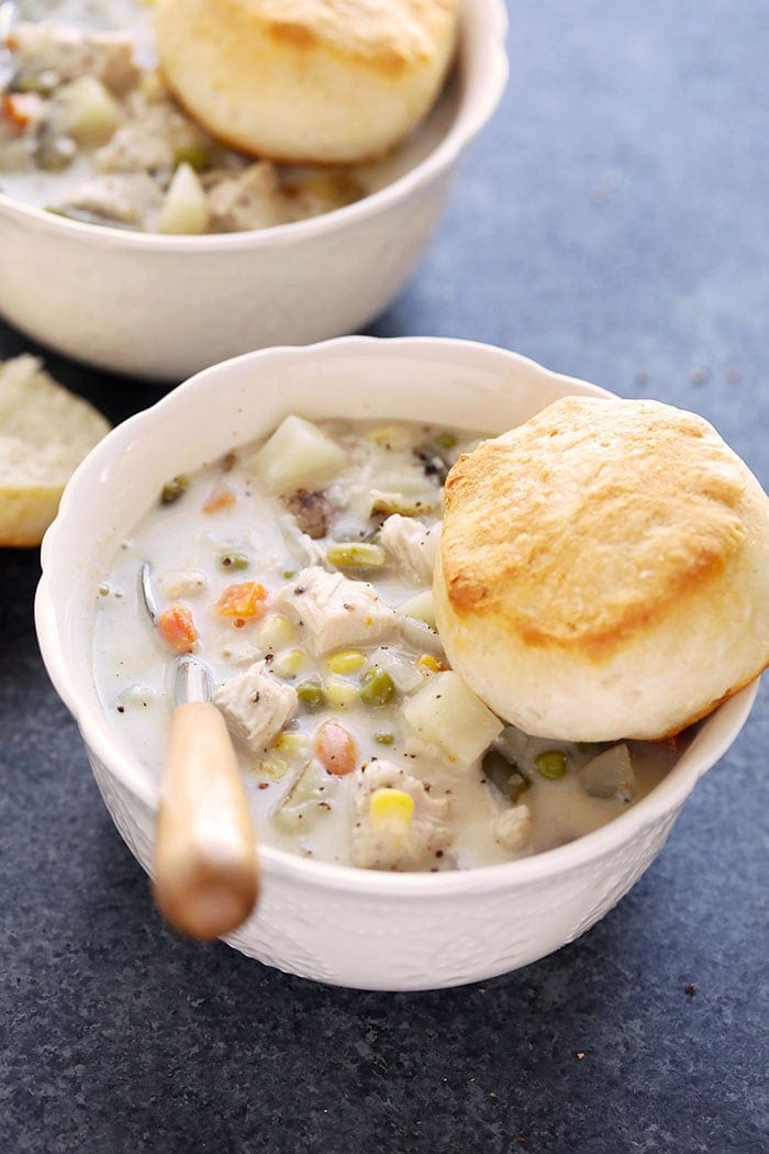 Slow cooker chicken pot pie soup in a bowl with a biscuit.