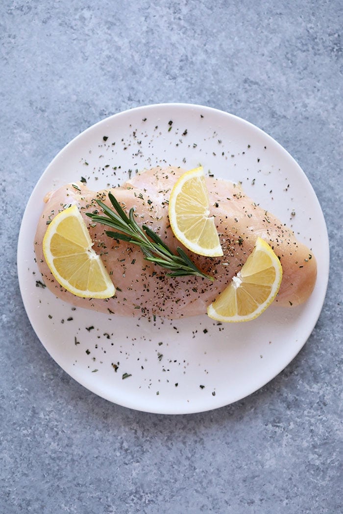 raw chicken breast on a square with lemon and rosemary.