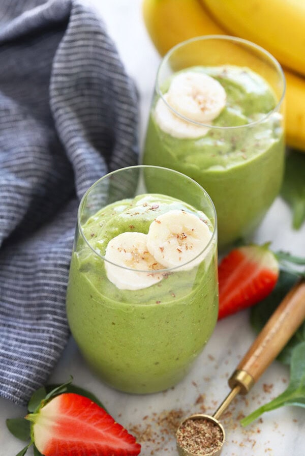 two glasses of green smoothie with bananas and strawberries.