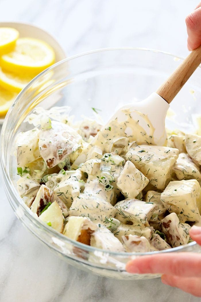 A hand mixing vegan potato salad in a bowl.