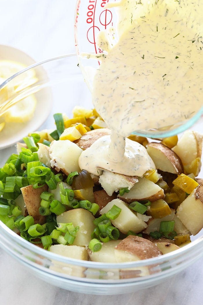 Pouring sauce over vegan potato salad ingredients