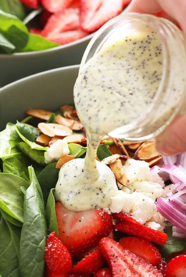 pouring poppy seed dressing on to salad.