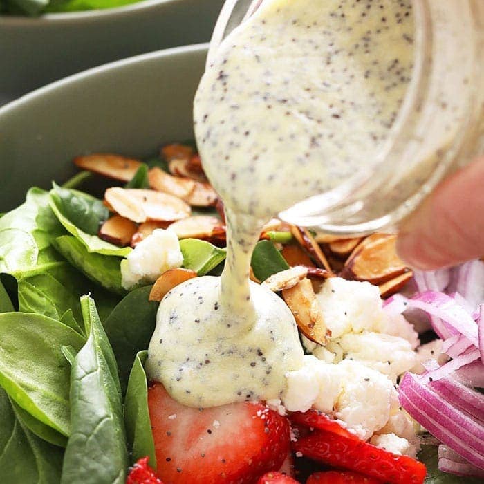 Pouring poppy seed dressing over a salad.